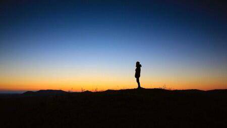 person looking out to the sunset atop a mountain